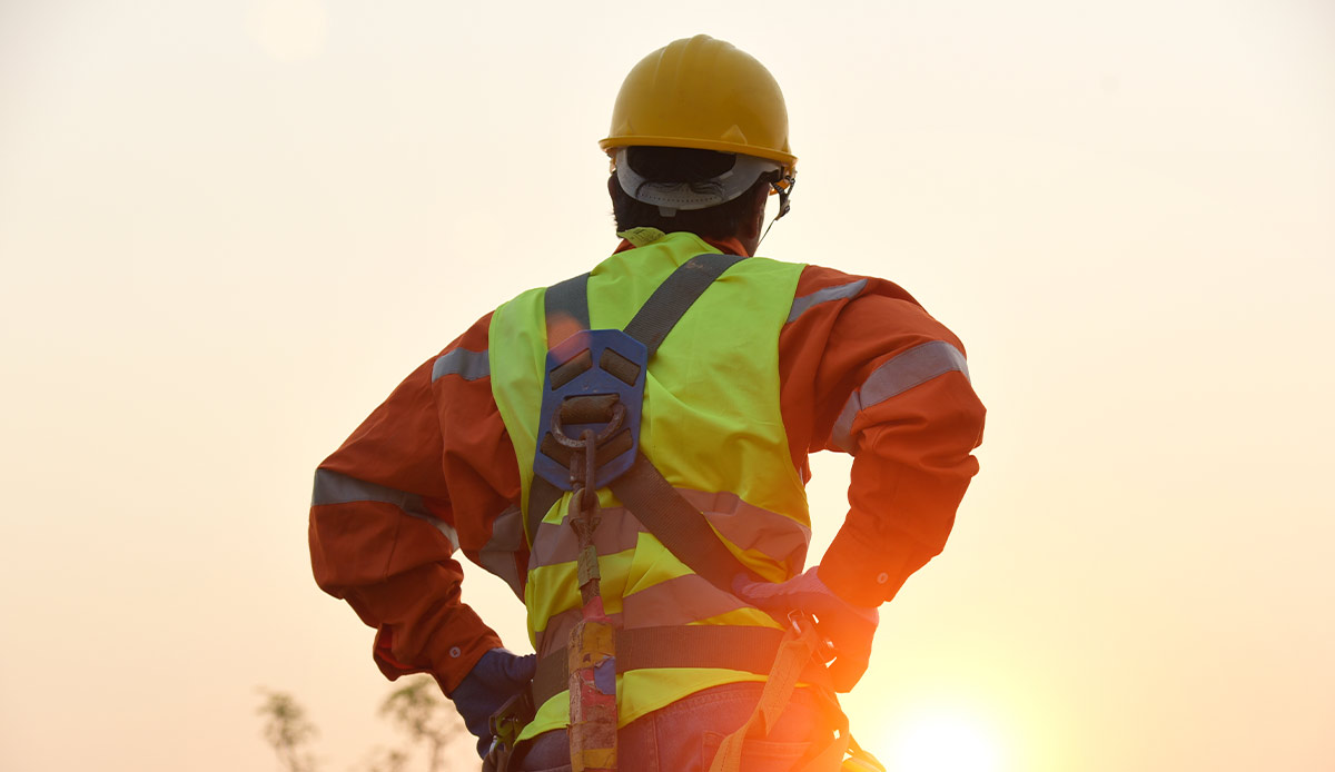An image of a man wearing construction garb looking into the sunlight of the work day coming to an end.